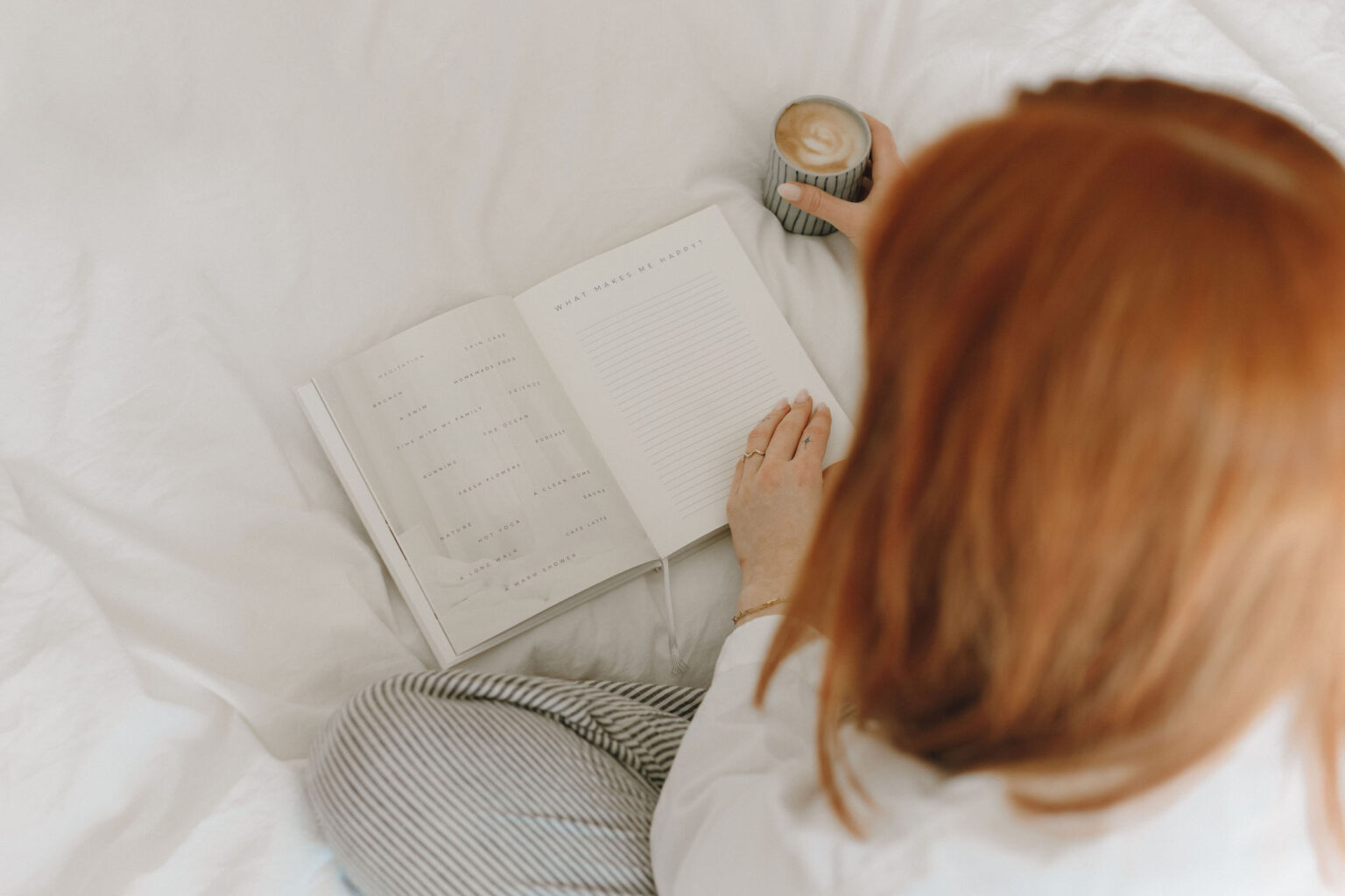 Kvinde der skriver i sin journal i sengen med en kop kaffe