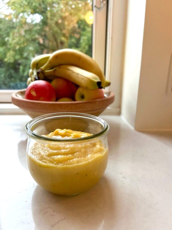 Hjemmelavet banan mango puré med bananer og frugt i baggrunden